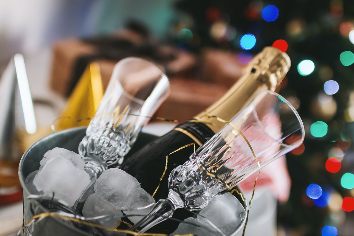 An uncorked bottle of champagne and two champagne flutes on ice in a festive New Year’s Eve setting.